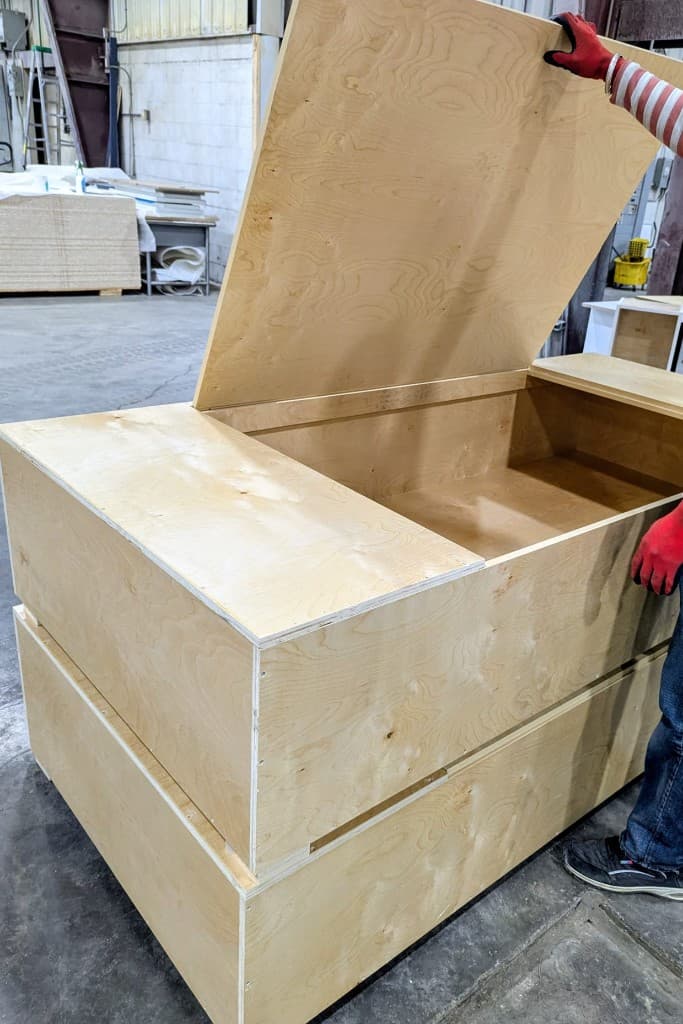 Craftsman opening the hinged storage lid of a custom-built box bed